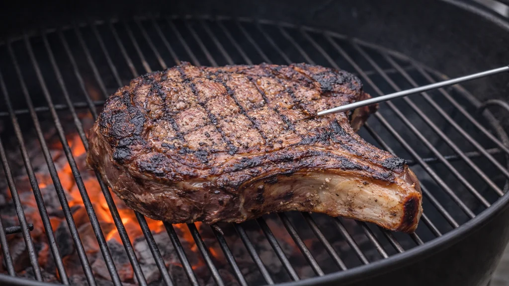 Côte de bœuf au barbecue en cuisson indirecte avec thermomètre à viande et braises visibles sous la grille